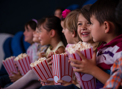 Happy group of kids at the cinema eating popcorn