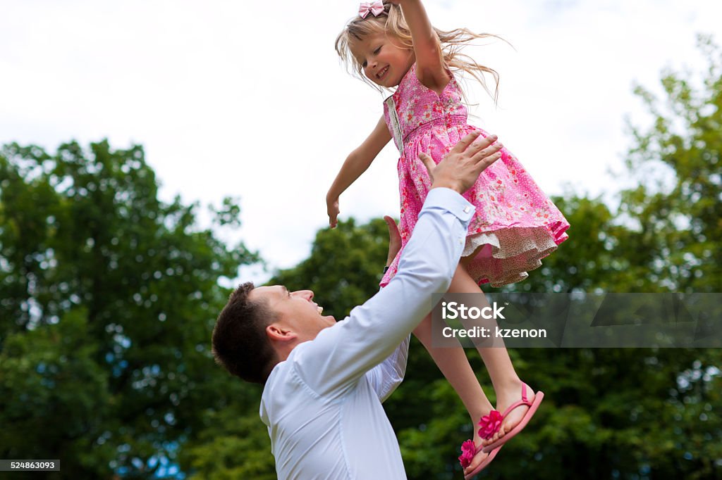 Father is playing with his daughter on a meadow Family affairs - father and daughter playing in summer; he is throwing her into the air Activity Stock Photo