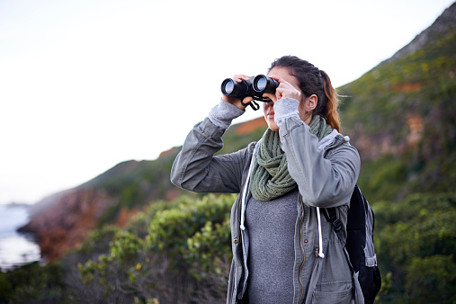 Shot of an attractive young woman using binoculars while out hiking