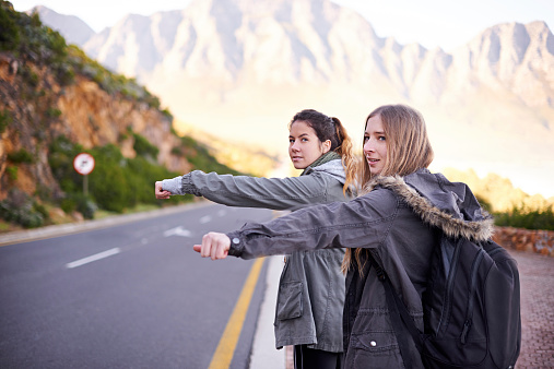 Cropped view of two young women hitchhiking along a mountainside road