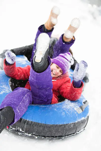 Two sisters, teenager girl and little girl, sliding at the slope and have fun with snowtubing at the winter resort 