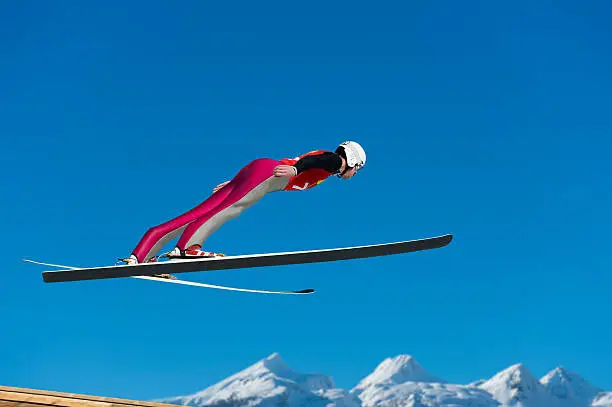Side view of young male ski jumper during the long ski jump against the sky and mountains