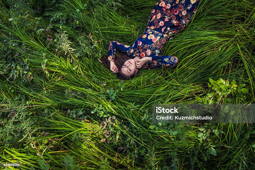 Beautiful young woman in dress lying in the grass Beautiful young woman in dress lying in the grass in nature Women Stock Photo