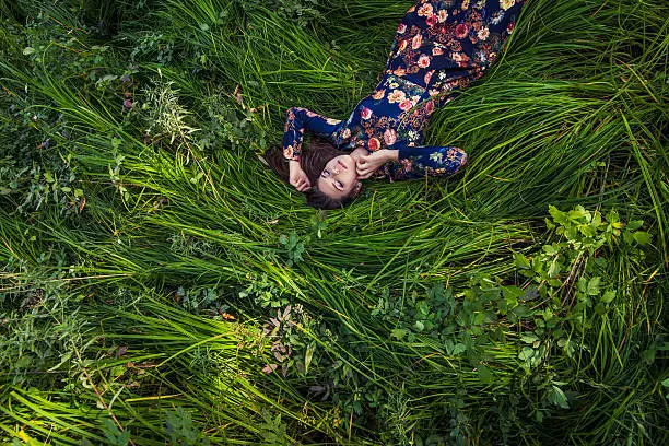 Beautiful young woman in dress lying in the grass in nature