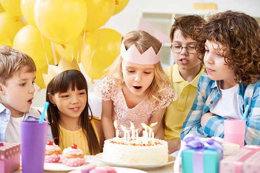 Little girl blowing out birthday candles surrounded by her friends