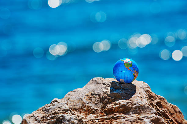 horizontal shot of earth sphere on rocks with the sea side in background.