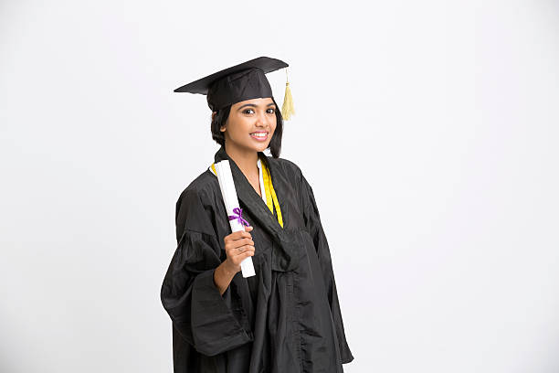 Happy young Indian girl college graduate Indian girl college graduate wearing cap and gown holding diploma and showing success sign on white south indian lady stock pictures, royalty-free photos & images