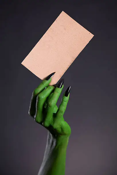 Green monster hand holding blank piece of cardboard, horror Halloween theme