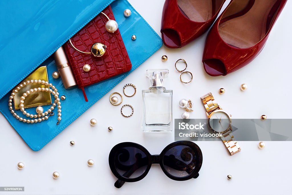 Overhead of essentials for modern young stylish woman. Fashionable female accessories watch sunglasses lipstick blue clutch and red shoes . Overhead of essentials for stylish young woman. Personal Accessory Stock Photo