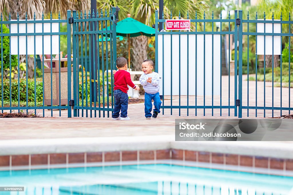 Terrible two's!. Twin boys get into a gate to pool Terrible two's times two!  Two year old afro american twin boys have gotten through a closed gate to a swimming pool.   Shot taken with a Canon 5D Mark 3 camera.  RM 18-23 Months Stock Photo