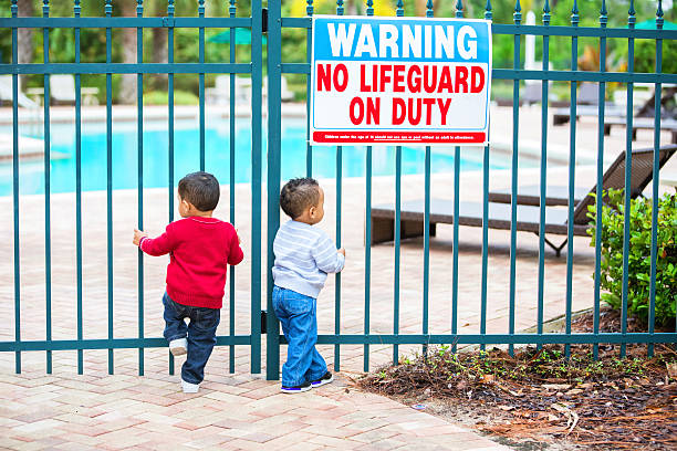 Double trouble. Twin boys try to get into locked pool Terrible two's times two! Two year old afro american twin boys are trying to get into a locked gate to a swimming pool. Sign says "Warning No Lifeguard on Duty". pool gate stock pictures, royalty-free photos & images