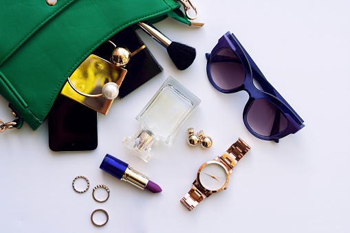 Top view of female fashion accessories for woman. Stylish sunglasses, green bag , gold watch , lipstick , perfume , rings , smartphone