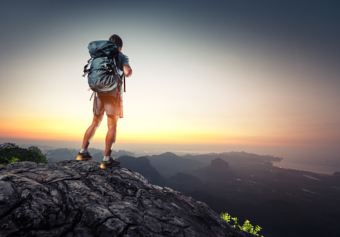 Hiker with backpack standing on top of a mountain and enjoying sunrise