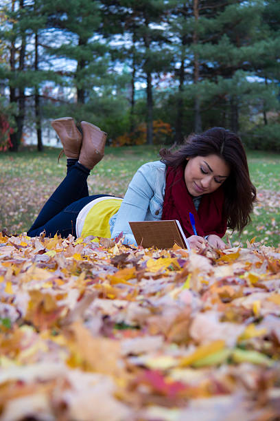 Girl writing in notebook lying down on colorful autumn lea stock photo