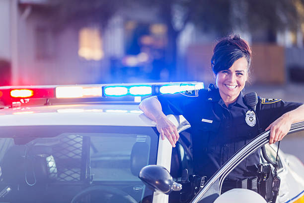 Female police officer standing next to patrol car A female police officer getting out of her patrol car. She is smiling, looking at the camera, leaning one arm on the open door of the vehicle. The lights are on. police officer stock pictures, royalty-free photos & images