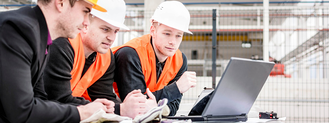 Architect and Construction Worker Checking Plans on Laptop.