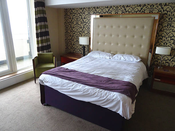 istock Kingsize double bed, large beige studded leather headboard, white-sheets, bedside-lamps 524925809