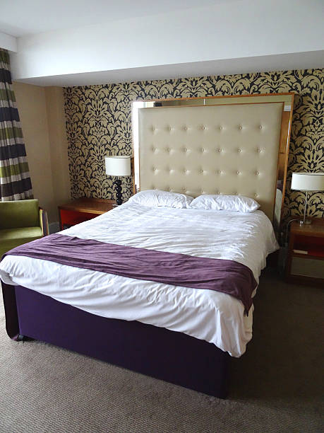istock Kingsize double bed, large beige studded leather headboard, white-sheets, bedside-lamps 524925811