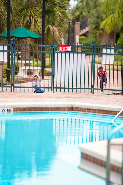 Double trouble. Twin boys try to get into locked pool Terrible two's times two! Two year old afro american twin boys are trying to get into a locked gate to a swimming pool. Sign says "Keep Gate Closed". pool gate stock pictures, royalty-free photos & images