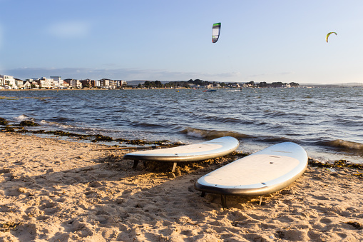Two surfboard on beach, windsurfers in background