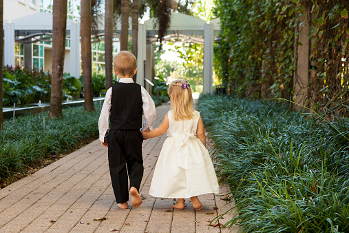 Young children dressed as bride and groom, walking down a path.