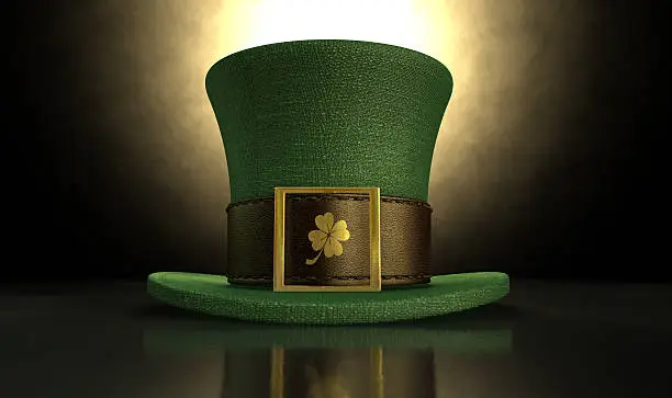 A green material leprechaun hat with a brown leather band emblazened with a gold shamrock and buckle on a dark spotlit background