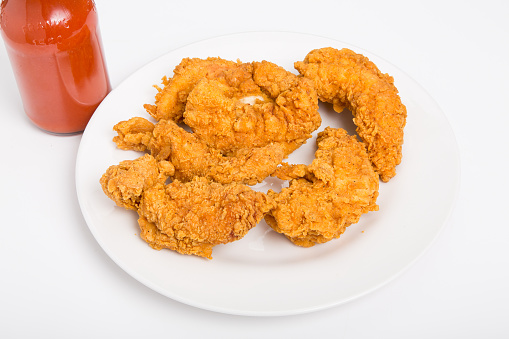 Hot, crispy chicken strips on a white plate with hot sauce