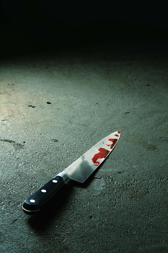 A bloody knife on a concrete floor with the killer looming over. 