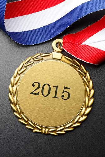 A gold medal engraved with the year 2015 on a black formica background.