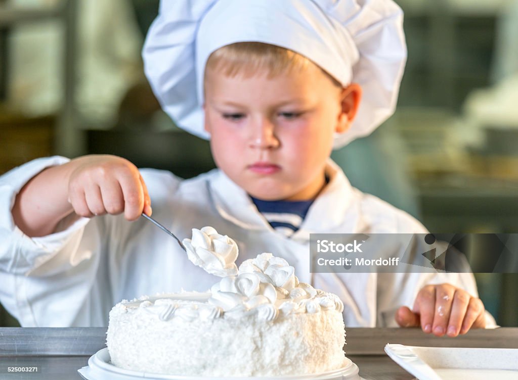 Sooking cake Nice boy confectioner decorating cake in confectionery shop Apron Stock Photo