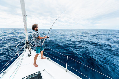 Young man fishing in open sea from sail boat