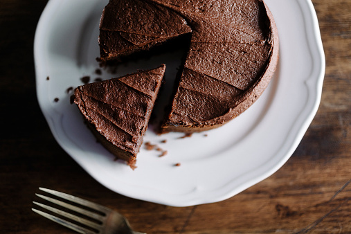 Whole sliced Chocolate cake with slice slightly removed. Photographed in window light with Nikon D800+50mm Zeiss Lens at ISO 100. Image Processed from raw file with VSCO Film Kodak Portra film simulation with film grain for a slightly more lo-fi look.