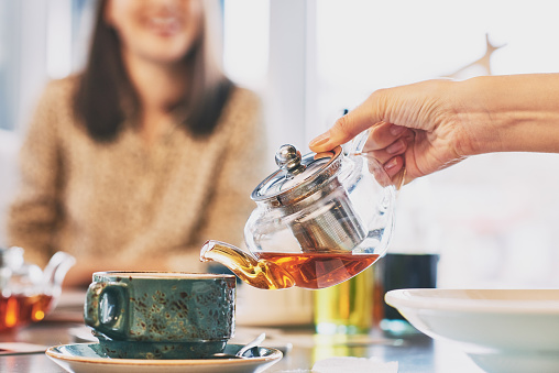 Female hands holding teapot with black tea and pouring it in cup
