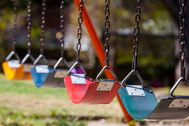 leere bunte schaukeln auf den park - kinderspielplatz stock-fotos und bilder