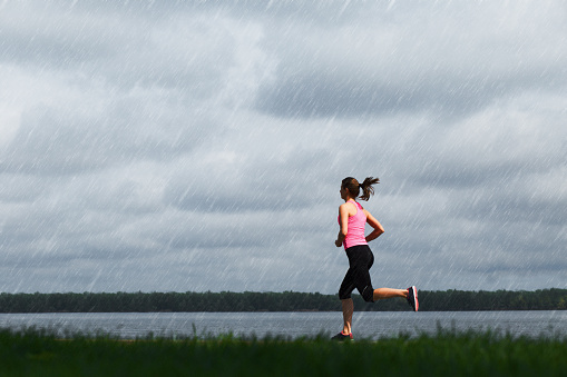 Young sporty woman running at rainy day