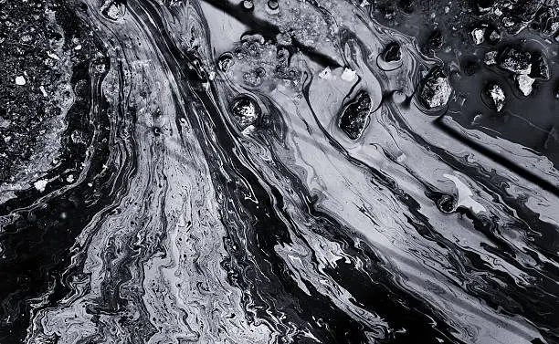 Abstract of an industrial chemical oil spill on the water surface releasing streaks of hazardous pollutants into the environment.