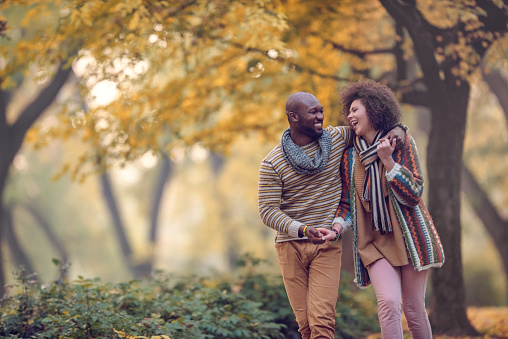 Cheerful embraced African American couple having fun and laughing while walking in nature during autumn.