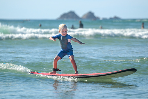 A little kid surfing and having fun on a red surfboard in clear and crystal water in Byron Bay, Australia