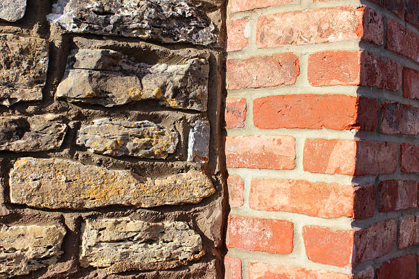 Photo showing a formal red-brick gate post, contrasting with an adjacent old cobblestone wall that has recently been repaired and repointed.  The brick post is one of a pair that stand either side of a gate / gateway, to form a simple, yet grand entrance to the house.