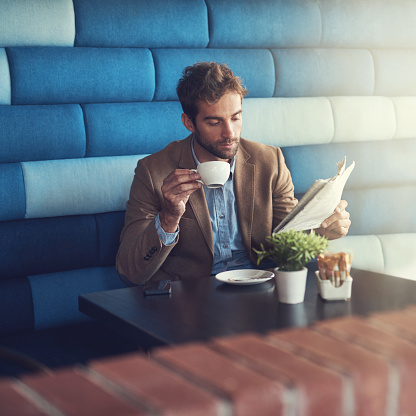 Shot of a handsome man reading a newspaper on a coffee creak in a cafe