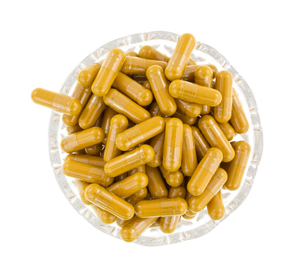 Top view of a group of turmeric herbal capsules in a small glass bowl on a white background.