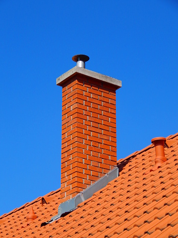 chimney in bright tile roof  with brick sunlight, against a blue sky