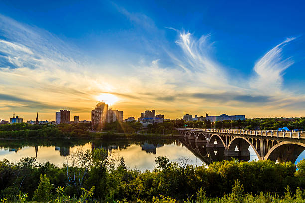 A warm summer sunset over the city of Saskatoon located in Central Canada where the calm waters of the South Saskatchewan River flows under the University Bridge.