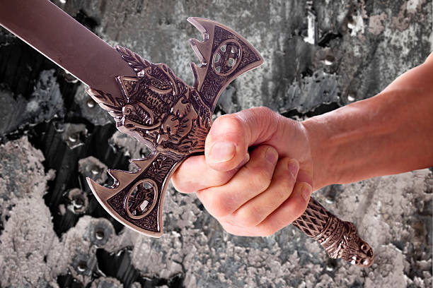 Man holds medieval sword. Rock background. Close-up of hand.