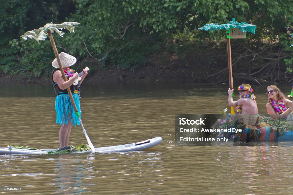 Anything That Floats Down the French Broad River Asheville; North Carolina; USA - August 9; 2014: Woman singing and playing a ukelele floats down the French Broad River on a surfboard with a palm tree paddle near other people floating on a palm tree island-like raft in the annual "Anything That Floats Race" on August 9; 2014 in Asheville; North Carolina North Carolina - US State Stock Photo
