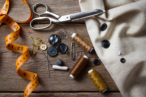 Sewing equipment like thread, needle, tape measure, scissors ,button, thimble and thread opener of blue fabric.