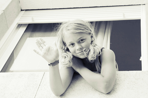 Young blond Caucasian girl showing hello gesture in the window, outdoor closeup monochrome portrait
