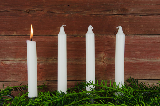 Four advent candles with one of them burning at a background of old red barn wall