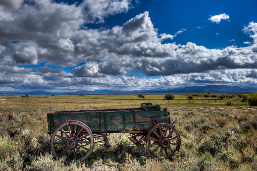 Isolated old covered wagon in field in rural Colorado with mountain background.