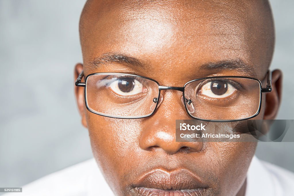 African male looking at the camera with a serious face. Close up of an african male looking at the camera with no emotion. Specs on his face and he is in front of a black chalk board. Cape Town, Western Cape, South Africa  Adult Stock Photo